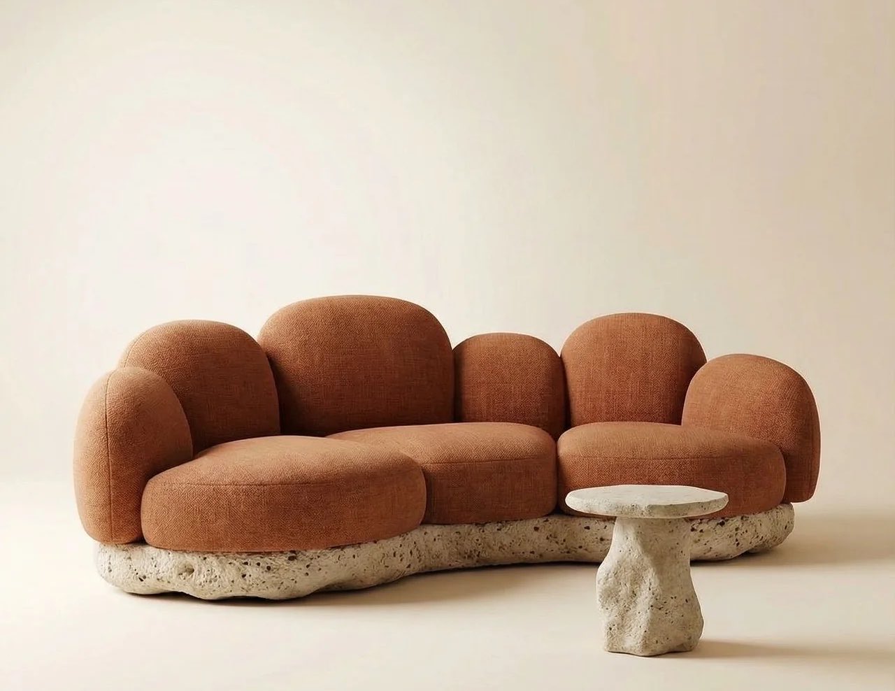 A rust bouclé sofa with rounded cushions resting on a rough stone base, beside a small stone side table
